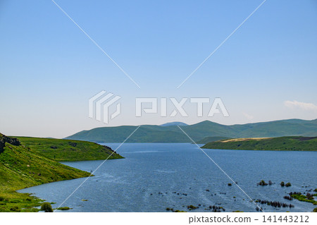 Serene lake surrounded by lush green hills and distant mountains Serene lake surrounded by lush green hills and distant mountains 141443212