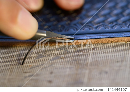 The hands of a craftsman finishing the edges of a leather belt. The hands of a craftsman finishing the edges of a leather belt. 141444107