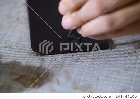 A leather craftsman's hands making sewing holes in leather with a four-pronged diamond awl. 141444109
