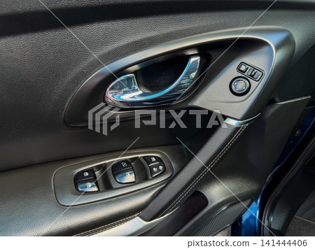 Details of a car door panel showing window controls and interior features in a vehicle parked indoors during daylight hours Details of a car door panel showing window controls and interior features in a vehicle parked indoors during daylight hours 141444406
