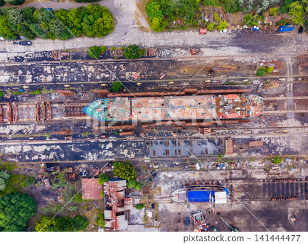 Ship docked at repair yard in a rusted condition with trees and buildings in surrounding area during daylight hours Ship docked at repair yard in a rusted condition with trees and buildings in surrounding area during daylight hours 141444477