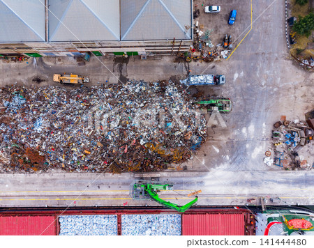 Large pile of scrap metal at recycling facility in urban area with several vehicles moving around during daylight hours Large pile of scrap metal at recycling facility in urban area with several vehicles moving around during daylight hours 141444480