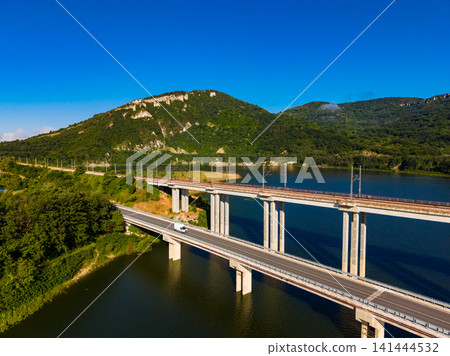 Bridges cross over a river with a truck traveling on a highway surrounded by hills and clear blue skies in a sunny setting Bridges cross over a river with a truck traveling on a highway surrounded by hills and clear blue skies in a sunny setting 141444532