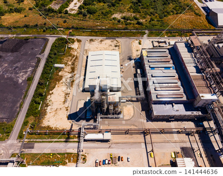 Industrial complex located near a road with large buildings and vehicles during daytime showing various structures and areas within the facility Industrial complex located near a road with large buildings and vehicles during daytime showing various structures and areas within the facility 141444636
