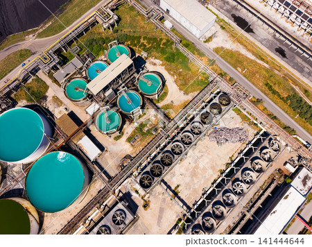 Water treatment facility operates in a large industrial area near a city with several holding tanks and pipes visible from above Water treatment facility operates in a large industrial area near a city with several holding tanks and pipes visible from above 141444644