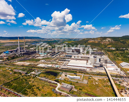 View of a large industrial facility from above with production buildings and smokestacks nearby in a rural setting during a clear day View of a large industrial facility from above with production buildings and smokestacks nearby in a rural setting during a clear day 141444655