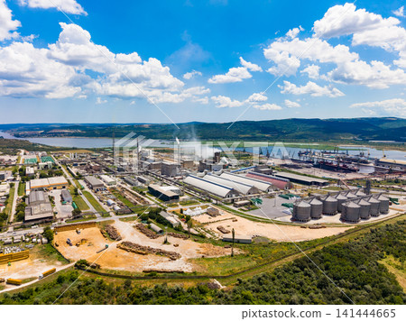 Industrial complex located near river with large buildings and silos under blue sky filled with clouds during daylight Industrial complex located near river with large buildings and silos under blue sky filled with clouds during daylight 141444665
