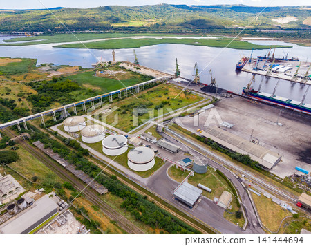 Industrial area with storage facilities and port near river during daytime in a rural location with hills in the background Industrial area with storage facilities and port near river during daytime in a rural location with hills in the background 141444694