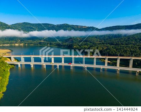 Bridges connect land across water at a location surrounded by green hills and a clear blue sky with some clouds Bridges connect land across water at a location surrounded by green hills and a clear blue sky with some clouds 141444924