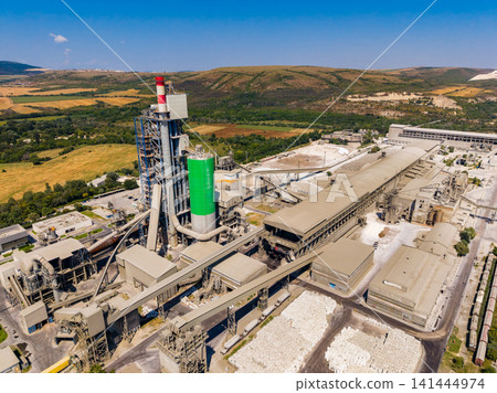 Industrial site shows cement production facility on a clear day in a rural area with hills and fields in the background Industrial site shows cement production facility on a clear day in a rural area with hills and fields in the background 141444974