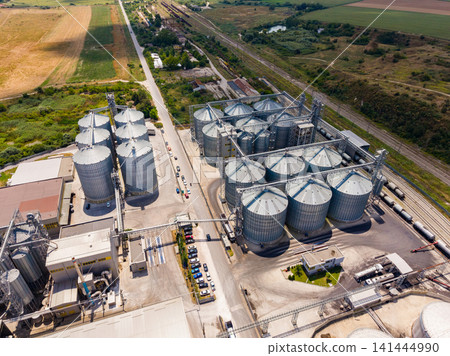 Large grain storage facility near a railway and fields during daylight hours Large grain storage facility near a railway and fields during daylight hours 141444990