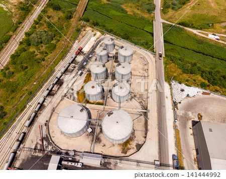 Storage tanks are located near a road and rail track in an industrial area with green fields in the background during daytime Storage tanks are located near a road and rail track in an industrial area with green fields in the background during daytime 141444992