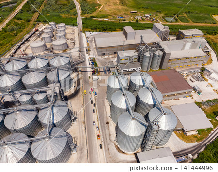 Industrial site with grain silos and processing buildings near a road in a rural area during bright daylight 141444996