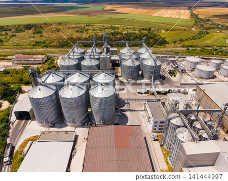 Multiple grain silos are seen from above in a farming area with green fields nearby during daylight hours Multiple grain silos are seen from above in a farming area with green fields nearby during daylight hours 141444997
