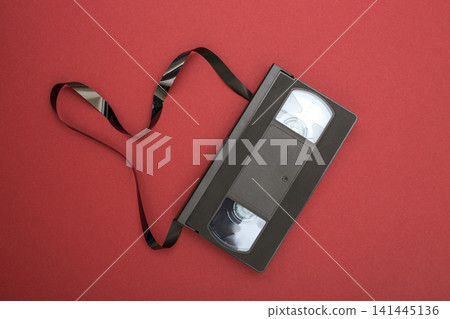 Video cassette with unrolled film on a red background 141445136