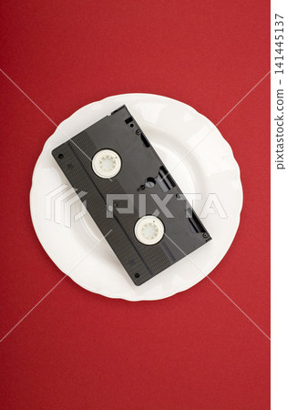 Video cassette on a white plate against a red background 141445137