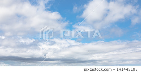 Sky with fluffy white cirrus clouds forming a soft atmospheric pattern. Natural background of blue sky with scattered white clouds and sunlight. Sky with fluffy white cirrus clouds forming a soft atmospheric pattern. Natural background of blue sky with scattered white clouds and sunlight. 141445195