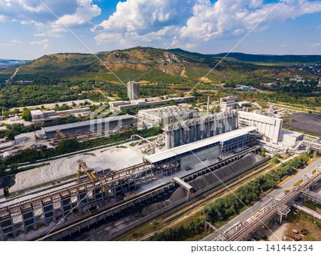 Industrial site with buildings and machinery under a blue sky near a mountain during daytime Industrial site with buildings and machinery under a blue sky near a mountain during daytime 141445234