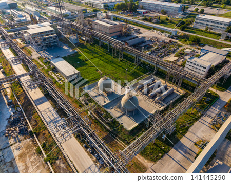 Industrial site with pipes and storage tanks located near a manufacturing area during daylight hours Industrial site with pipes and storage tanks located near a manufacturing area during daylight hours 141445290