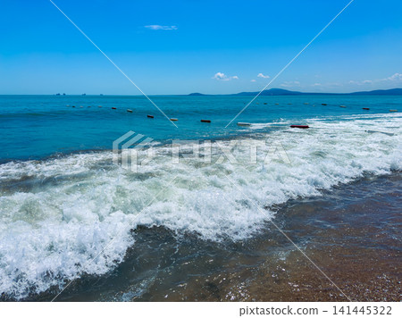 Waves crash on a sandy beach with blue water and a clear sky in a coastal area during the daytime Waves crash on a sandy beach with blue water and a clear sky in a coastal area during the daytime 141445322