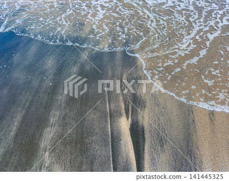 Waves gently reach the shore as the sun shines on wet sand during a clear day at the beach Waves gently reach the shore as the sun shines on wet sand during a clear day at the beach 141445325