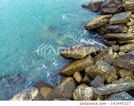 Waves wash over rocky shore with clear water at a coastal location during daylight hours Waves wash over rocky shore with clear water at a coastal location during daylight hours 141445327