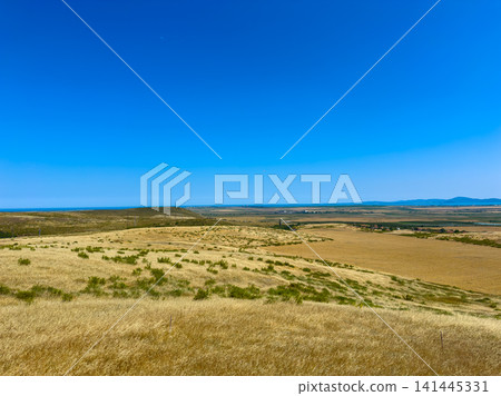 Wide open landscape showing fields and a distant view of a body of water under a clear blue sky during bright daylight hours Wide open landscape showing fields and a distant view of a body of water under a clear blue sky during bright daylight hours 141445331