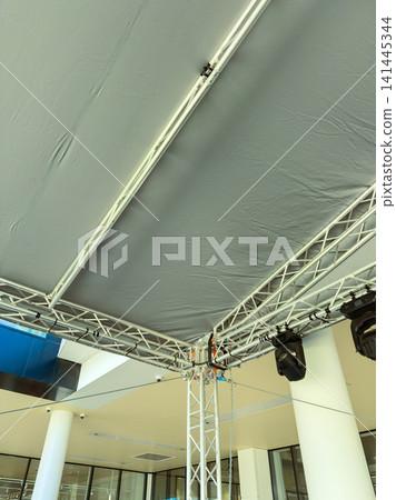 Setup of a stage with a gray canopy and lighting at an indoor venue during the daytime before an event 141445344