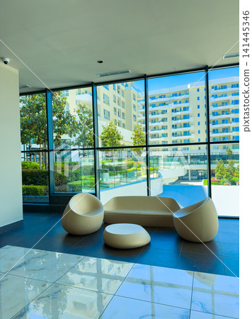 Modern seating area with large windows showing outdoor pool and buildings during daytime in a residential complex setting Modern seating area with large windows showing outdoor pool and buildings during daytime in a residential complex setting 141445346