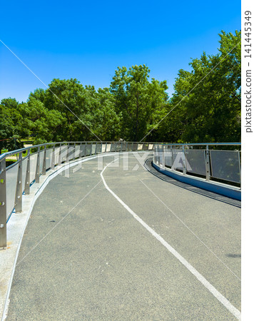 Walking path curves through green trees under a clear blue sky near a park in the summer Walking path curves through green trees under a clear blue sky near a park in the summer 141445349