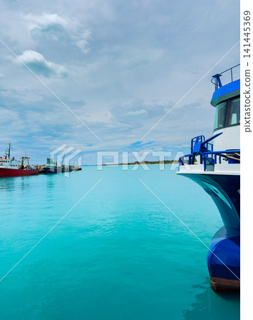 View of a blue boat near the shore with calm water and distant fishing boats under a cloudy sky during daytime View of a blue boat near the shore with calm water and distant fishing boats under a cloudy sky during daytime 141445369