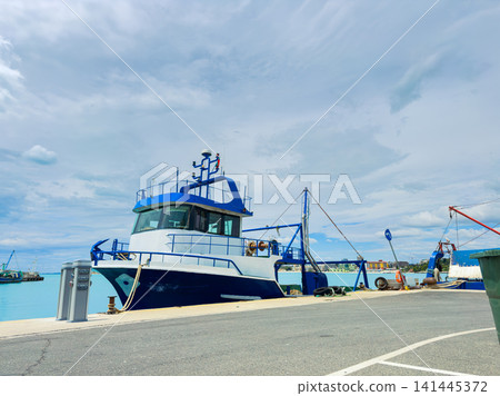 Fishing boat docked near the water under a cloudy sky with another boat in the background and a concrete path in the foreground Fishing boat docked near the water under a cloudy sky with another boat in the background and a concrete path in the foreground 141445372