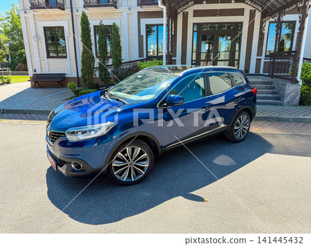 Blue SUV parked outside a large building with a green lawn and trees on a sunny day in a residential area Blue SUV parked outside a large building with a green lawn and trees on a sunny day in a residential area 141445432