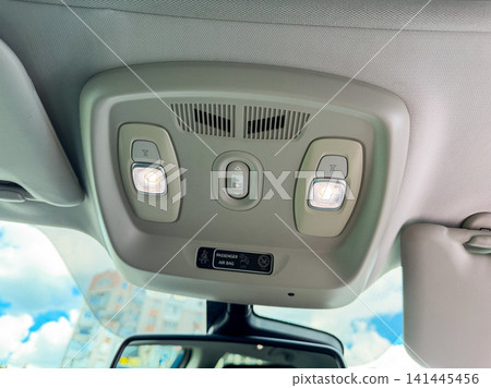 View of the interior roof panel of a car showing lights and buttons for features and controls at daytime with a blue sky outside View of the interior roof panel of a car showing lights and buttons for features and controls at daytime with a blue sky outside 141445456