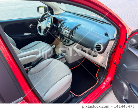 Interior view of a red car showing seats, dashboard, and controls during daytime in a parking area Interior view of a red car showing seats, dashboard, and controls during daytime in a parking area 141445475