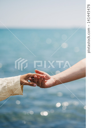 Two hands reach out to each other against the backdrop of the ocean on a sunny day near the shore 141445476