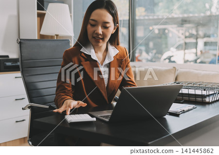 Asian businesswoman using calculator and working on laptop at modern office Asian businesswoman using calculator and working on laptop at modern office 141445862