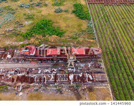 Abandoned ship and surrounding area with fields and debris in daytime near a dock 141445960