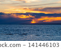 Sun sets behind dark clouds over deep blue sea. Beautiful orange sky with golden rays reflecting on water. Concept of hope and tranquility. Natural sunset background. 141446103