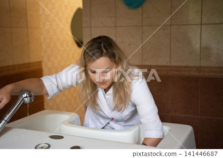 A professional fills a bathtub with water. She is wearing a white shirt and is working in a bathroom that is clean. 141446687