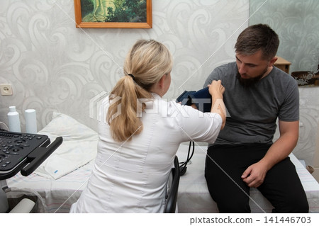 A doctor checks a man's blood pressure in an examination room, ensuring patient health with medical expertise and care. Routine checkup. A doctor checks a man's blood pressure in an examination room, ensuring patient health with medical expertise and care. Routine checkup. 141446703