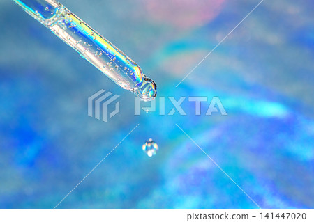 Macro shot of a glass dropper releasing a water droplet over an iridescent blue background for skincare Macro shot of a glass dropper releasing a water droplet over an iridescent blue background for skincare 141447020