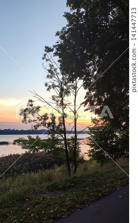 Golden sunset landscape featuring the Daugava River. Scenic Latvian city view combining wildlife, water, and architecture. Golden sunset landscape featuring the Daugava River. Scenic Latvian city view combining wildlife, water, and architecture. 141447713
