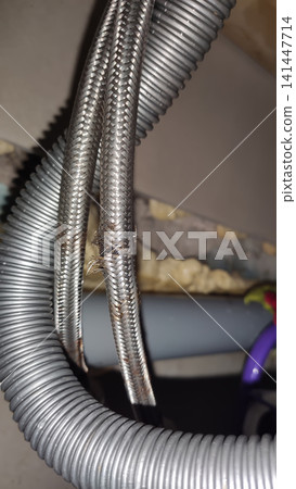 Damaged flexible hose with a metal braided sheath showing visible tears, corrosion, and signs of wear. Damaged flexible hose with a metal braided sheath showing visible tears, corrosion, and signs of wear. 141447714