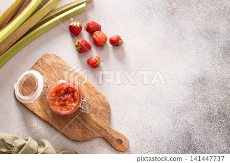 Homemade strawberry rhubarb jam in open glass jar on wooden board flat lay Homemade strawberry rhubarb jam in open glass jar on wooden board flat lay 141447737