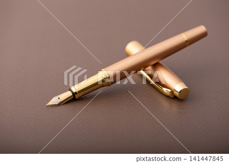 Fountain pen, beautiful fountain pen with detailed design on a brown synthetic leather surface, selective focus. Fountain pen, beautiful fountain pen with detailed design on a brown synthetic leather surface, selective focus. 141447845