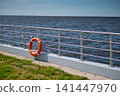 An orange-colored lifebuoy hangs on the embankment fence in sunny weather, finland gulf, with the sea in the background. 141447970