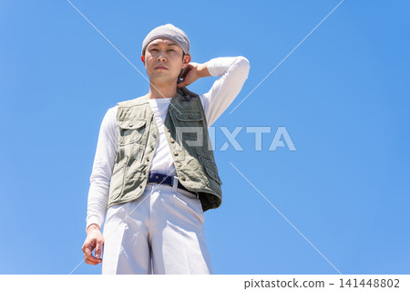 A male worker in work clothes stands against a blue sky. 141448802