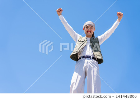 一名身穿工作服的男子在藍天下擺出勝利姿勢。 一名身穿工作服的男子在藍天下擺出勝利姿勢。 141448806