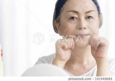A senior woman uses a facial steamer to perform a self-care facial. A senior woman uses a facial steamer to perform a self-care facial. 141449085